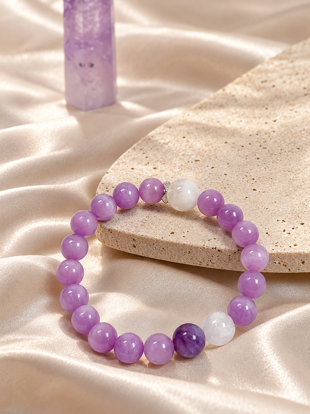 Natural Cat’s Eye Kunzite, Charoite and White Phantom Quartz bracelet resting on textured travertine stone and soft champagne silk, with gentle natural lighting and a serene, elegant atmosphere.