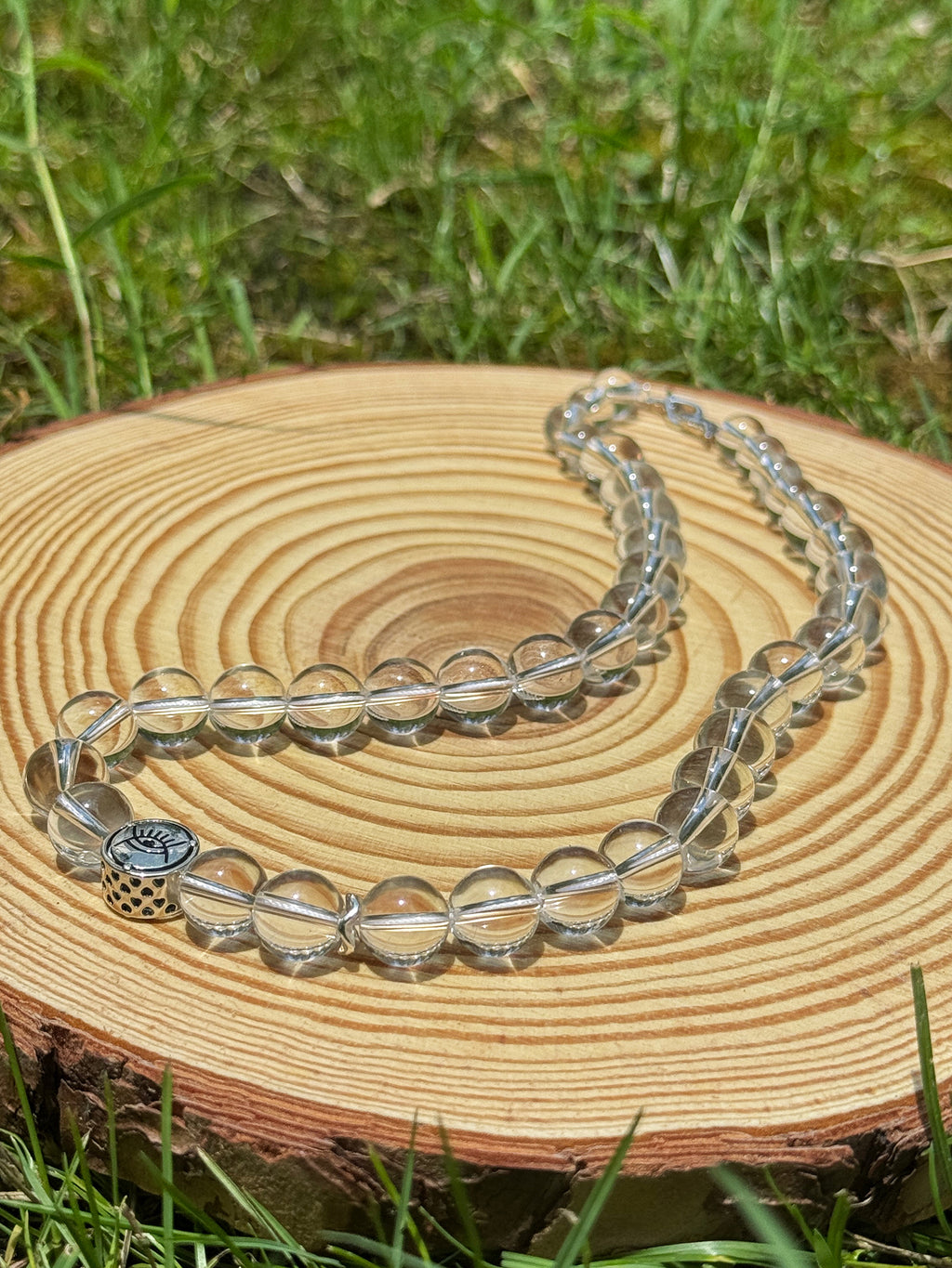 Clear quartz necklace displayed on natural wood outdoors in sunlight