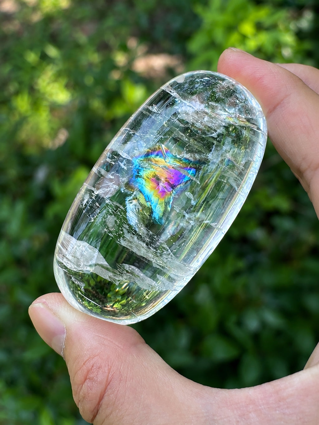 Natural clear quartz rainbow crystal held in hand under natural sunlight.

