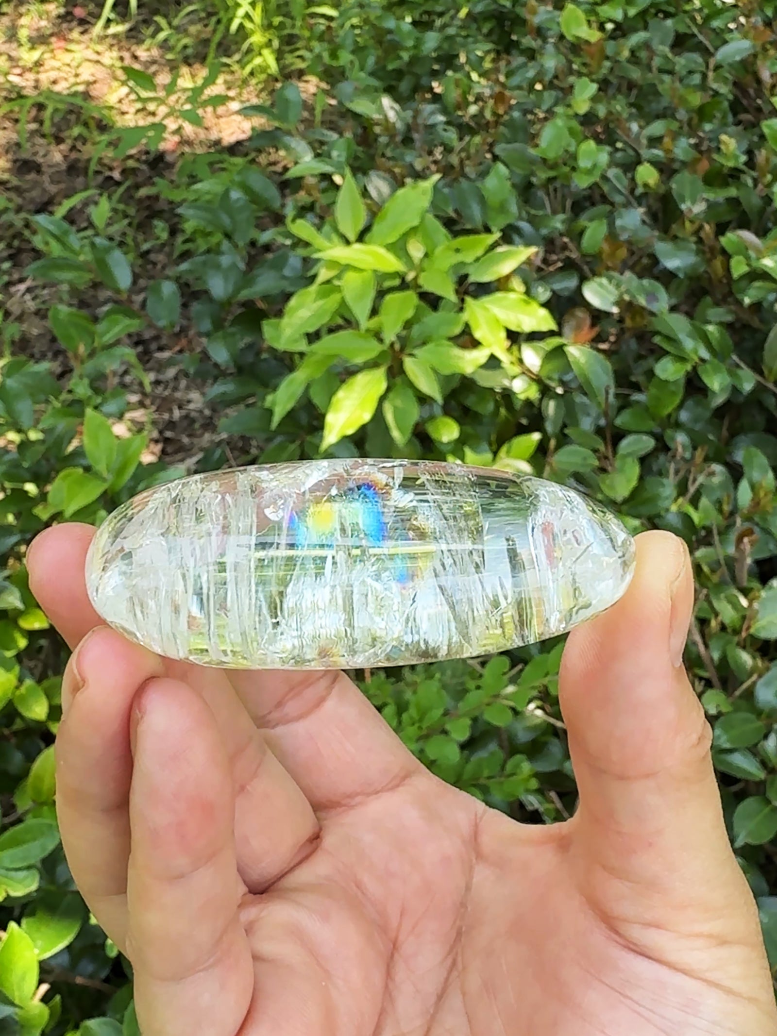 Side view of natural clear quartz rainbow crystal showing internal rainbow inclusions.