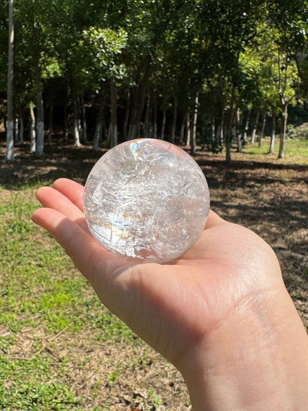 Clear quartz sphere held in hand under natural sunlight.
