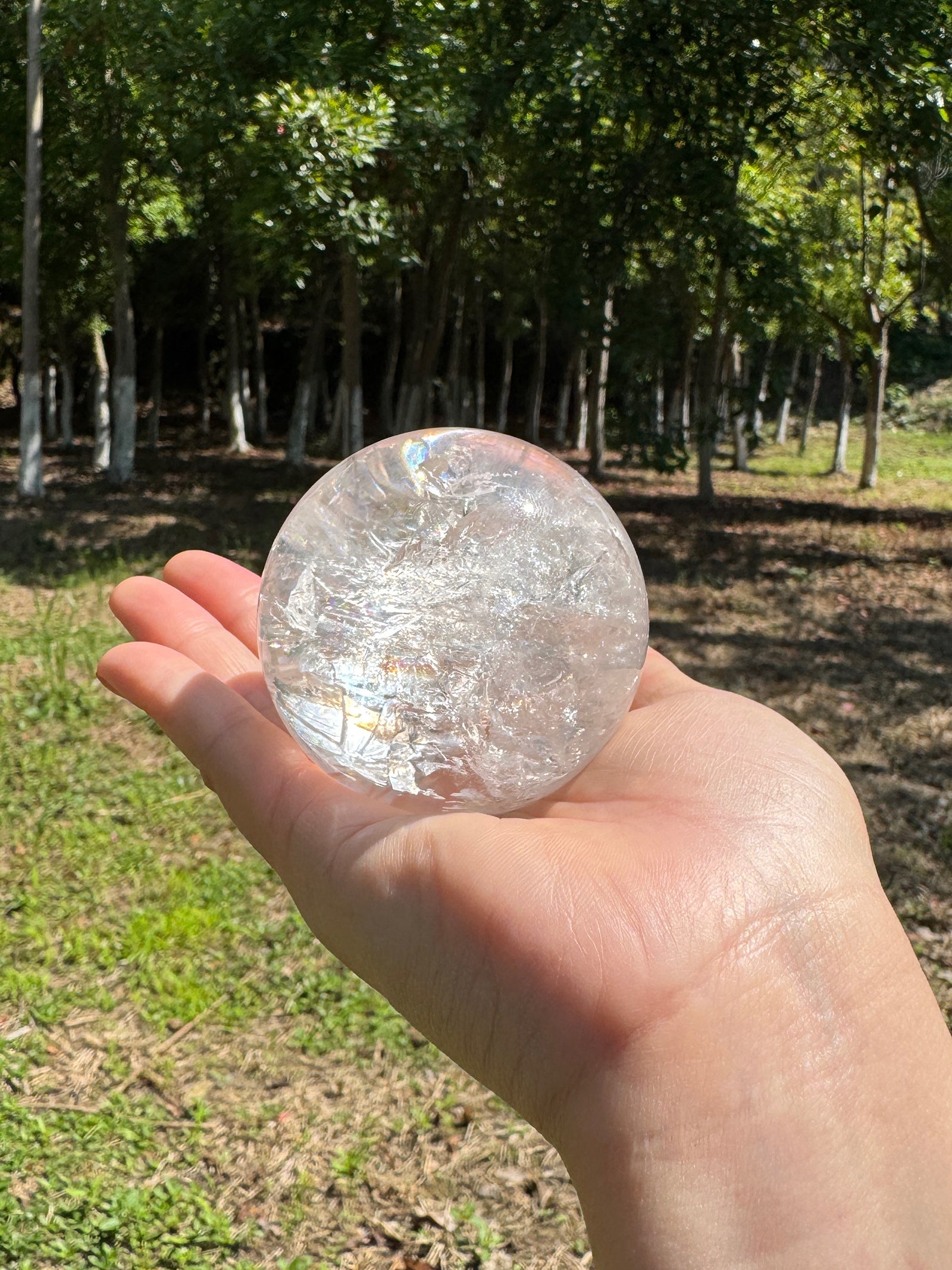 Clear quartz sphere held in hand under natural sunlight.
