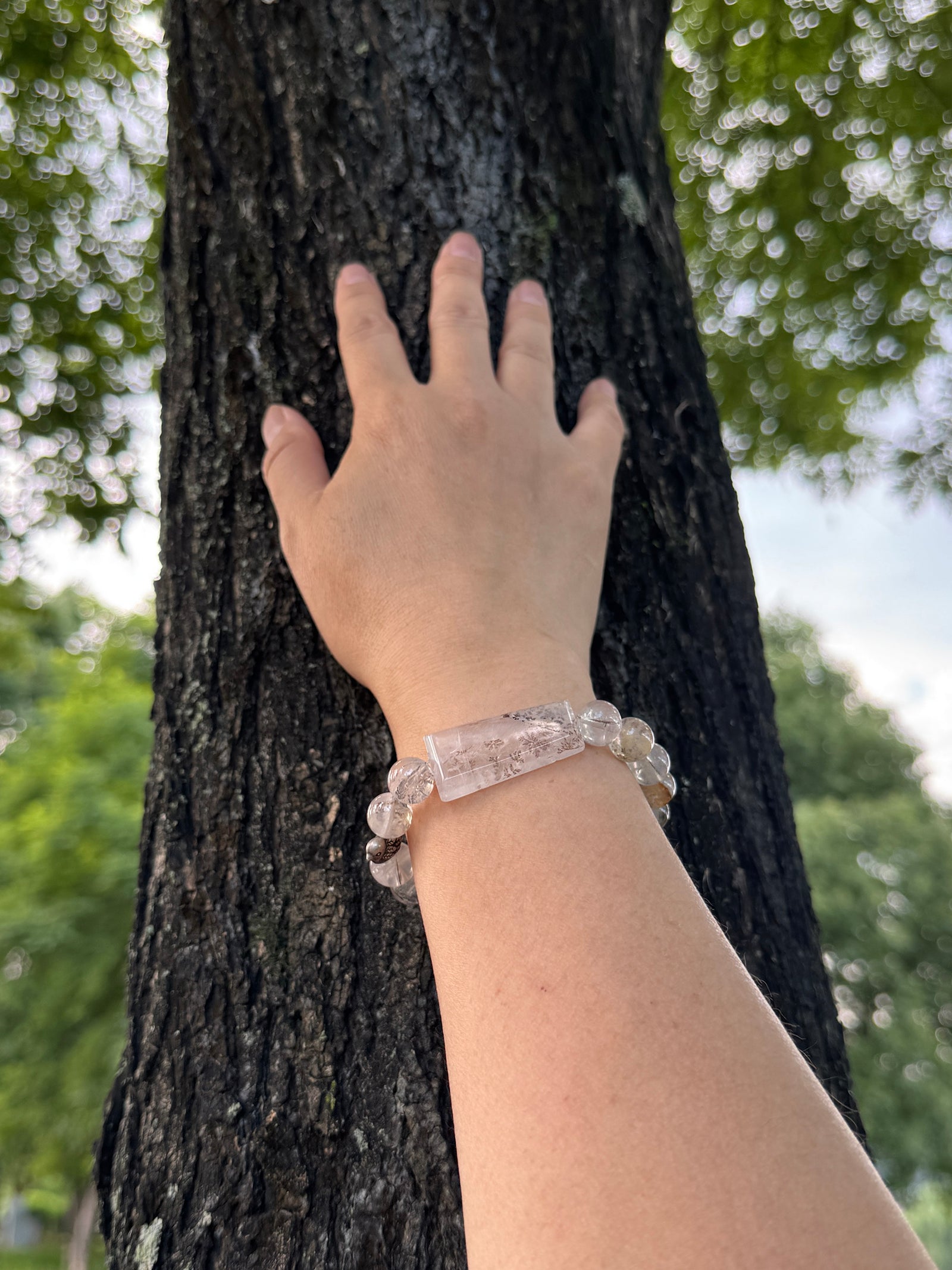 One of a Kind Dendritic Quartz bracelet worn on wrist surrounded by natural greenery