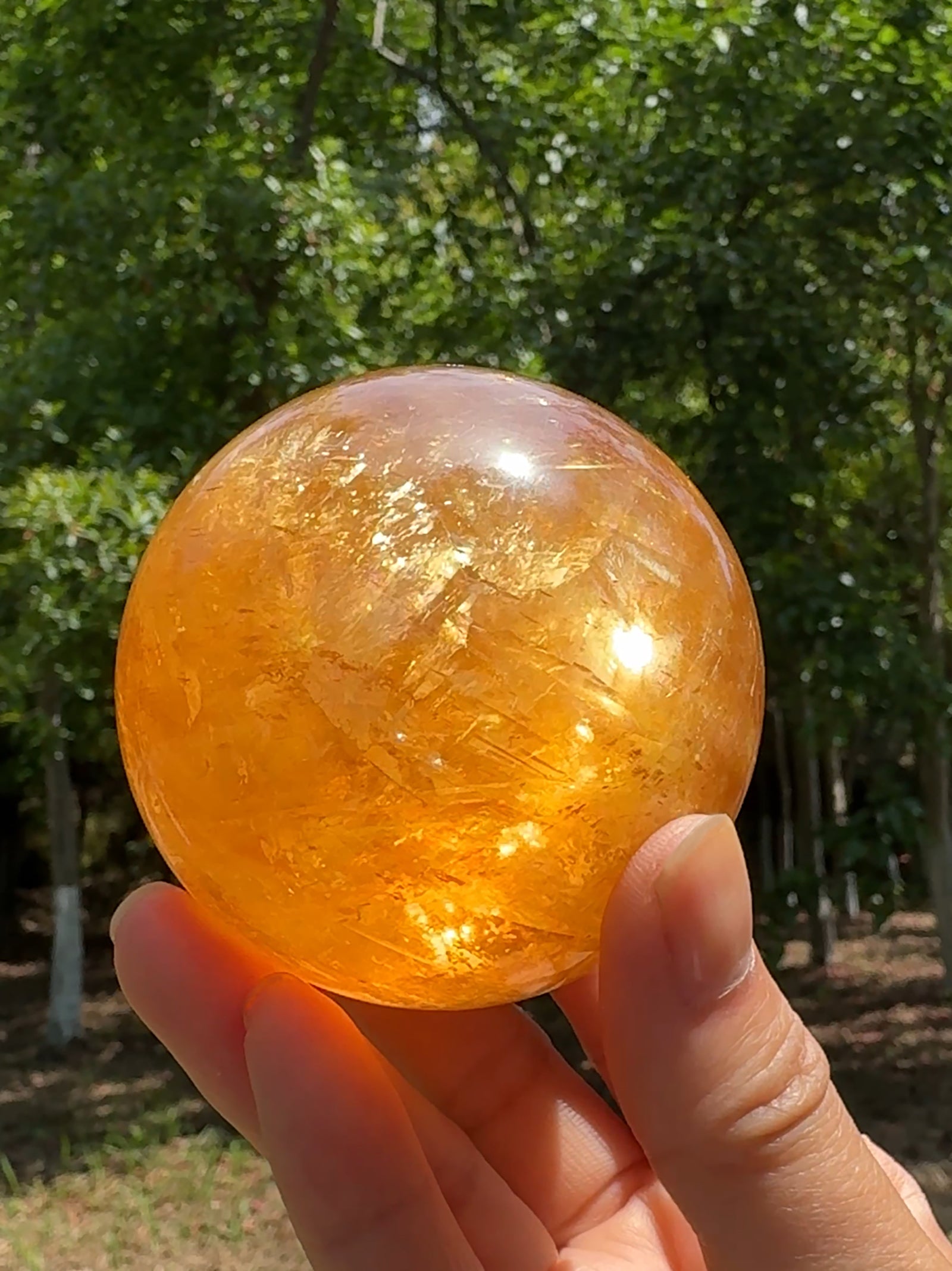 Full view of a natural honey calcite crystal sphere with warm golden tones, glowing translucency, and natural internal rainbows