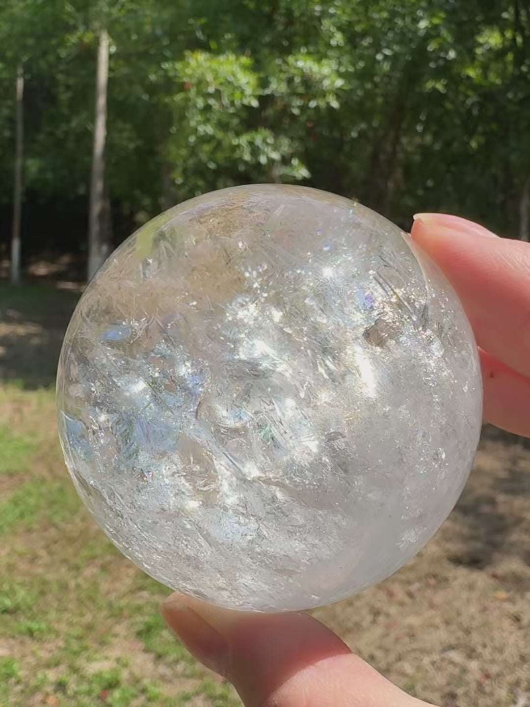 Himalayan clear quartz sphere glowing with shifting rainbow reflections in natural light.