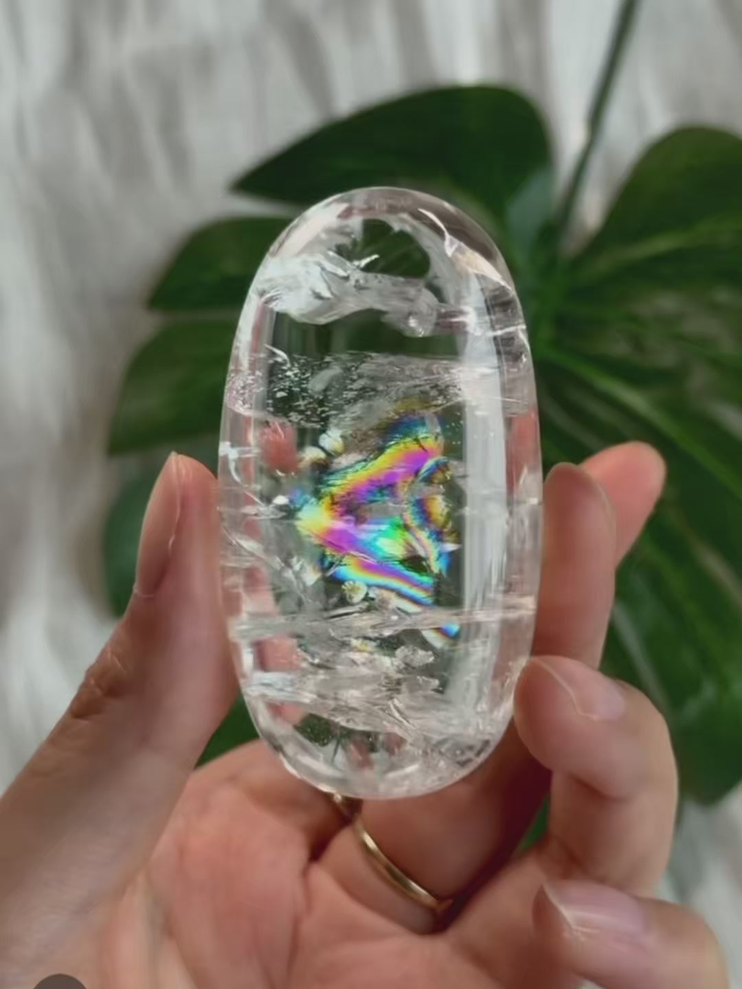 Hand-held natural clear quartz crystal displaying a vibrant rainbow under sunlight.