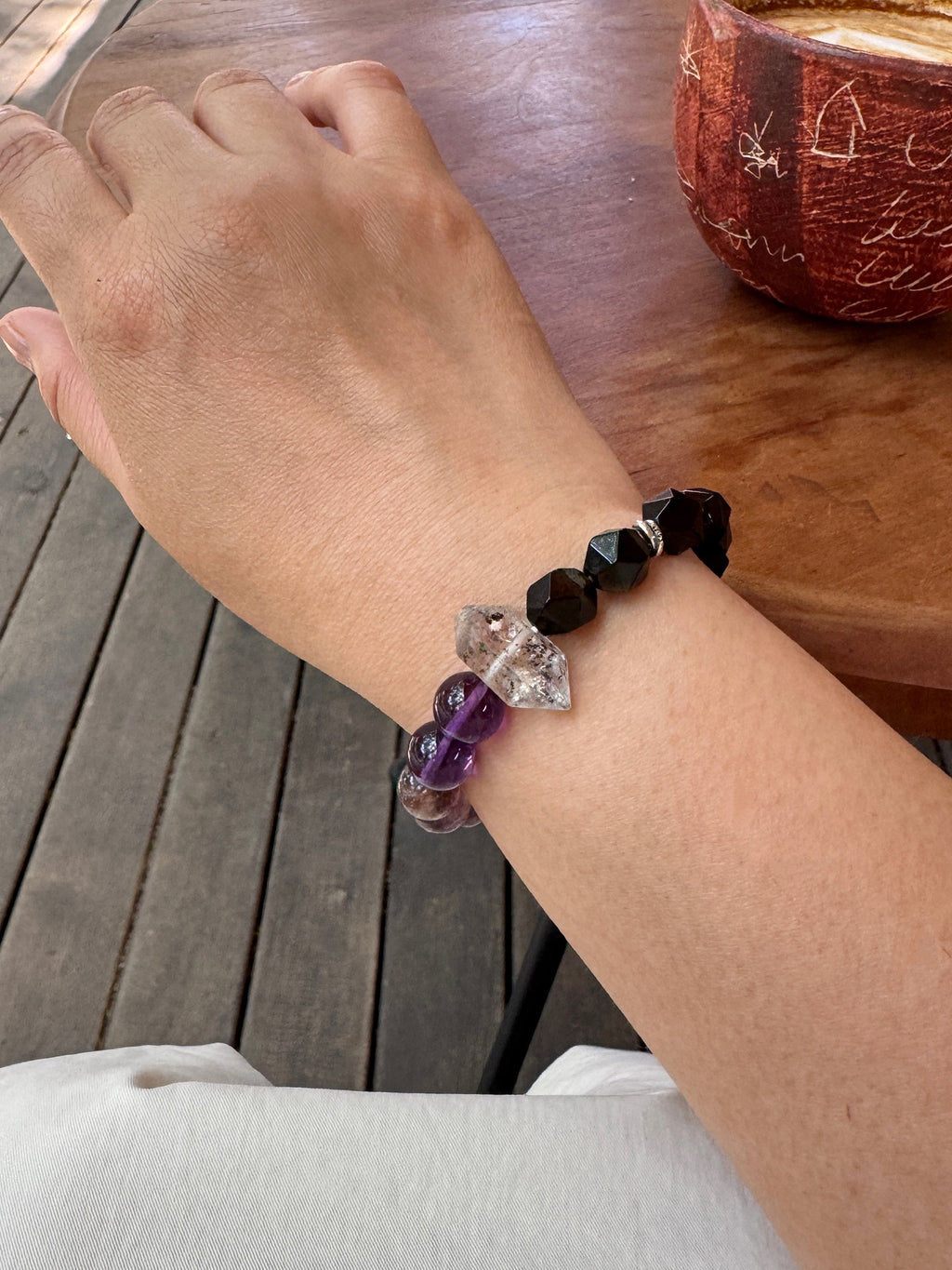 Purple titanium quartz, amethyst, and obsidian bracelet worn on wrist close-up showing layered violet tones and grounding crystal details
