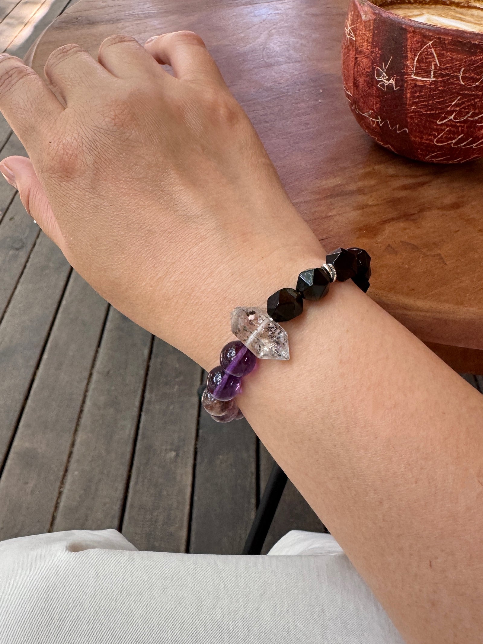 Purple titanium quartz, amethyst, and obsidian bracelet worn on wrist close-up showing layered violet tones and grounding crystal details