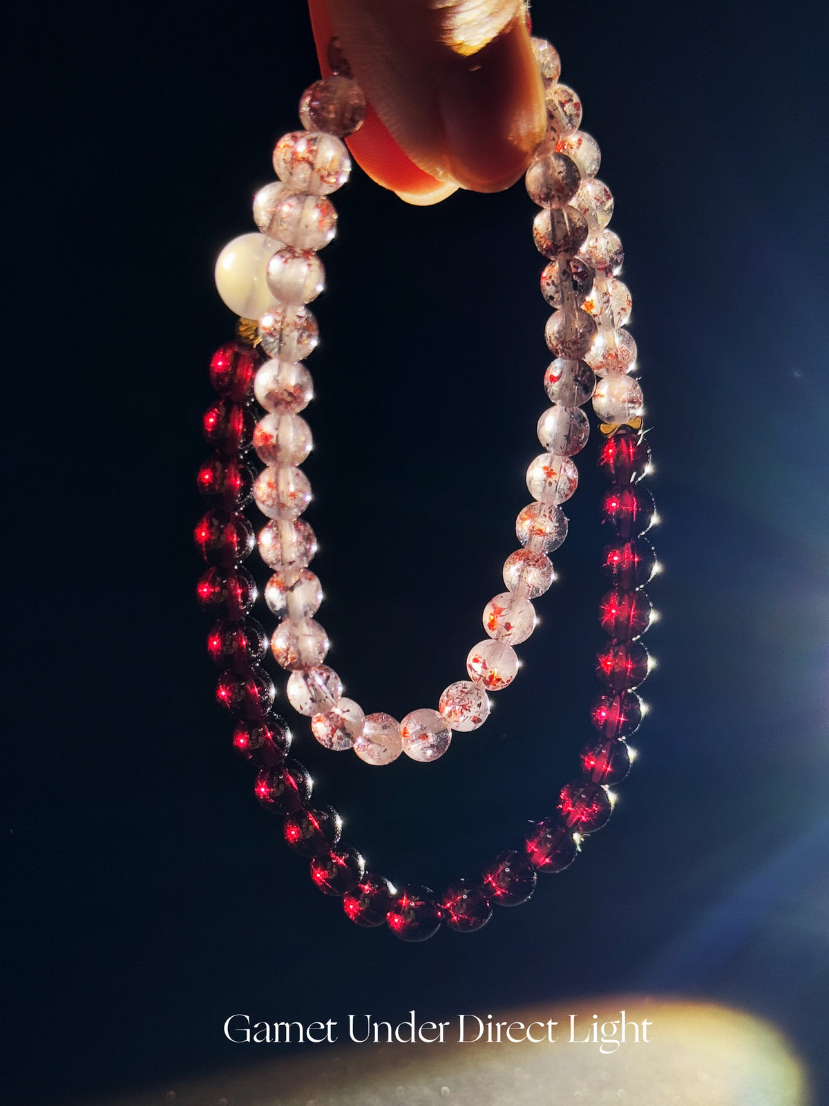 Red Super Seven, Garnet and Moonstone double-wrap bracelet featuring deep wine-red Garnet tones under direct lighting against a dark background.