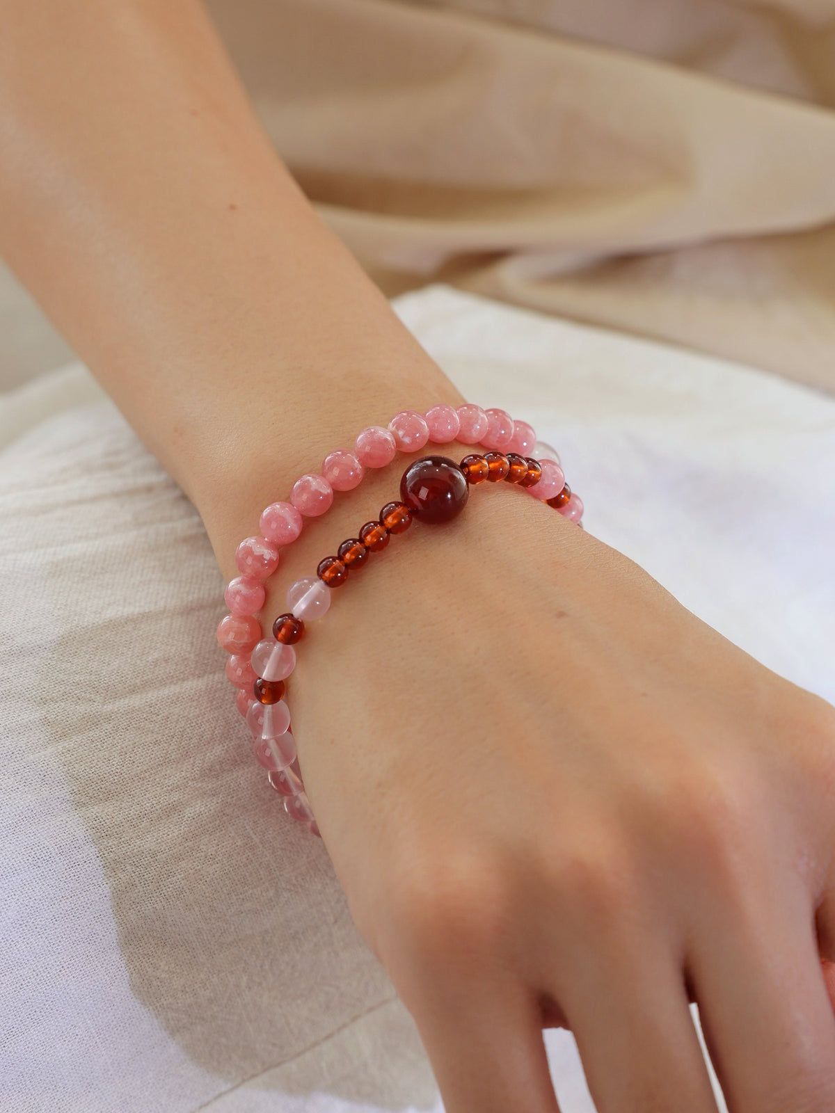 Close view of a double-wrap Rhodochrosite, Star Rose Quartz, and Orange-Red Garnet bracelet worn on the wrist.