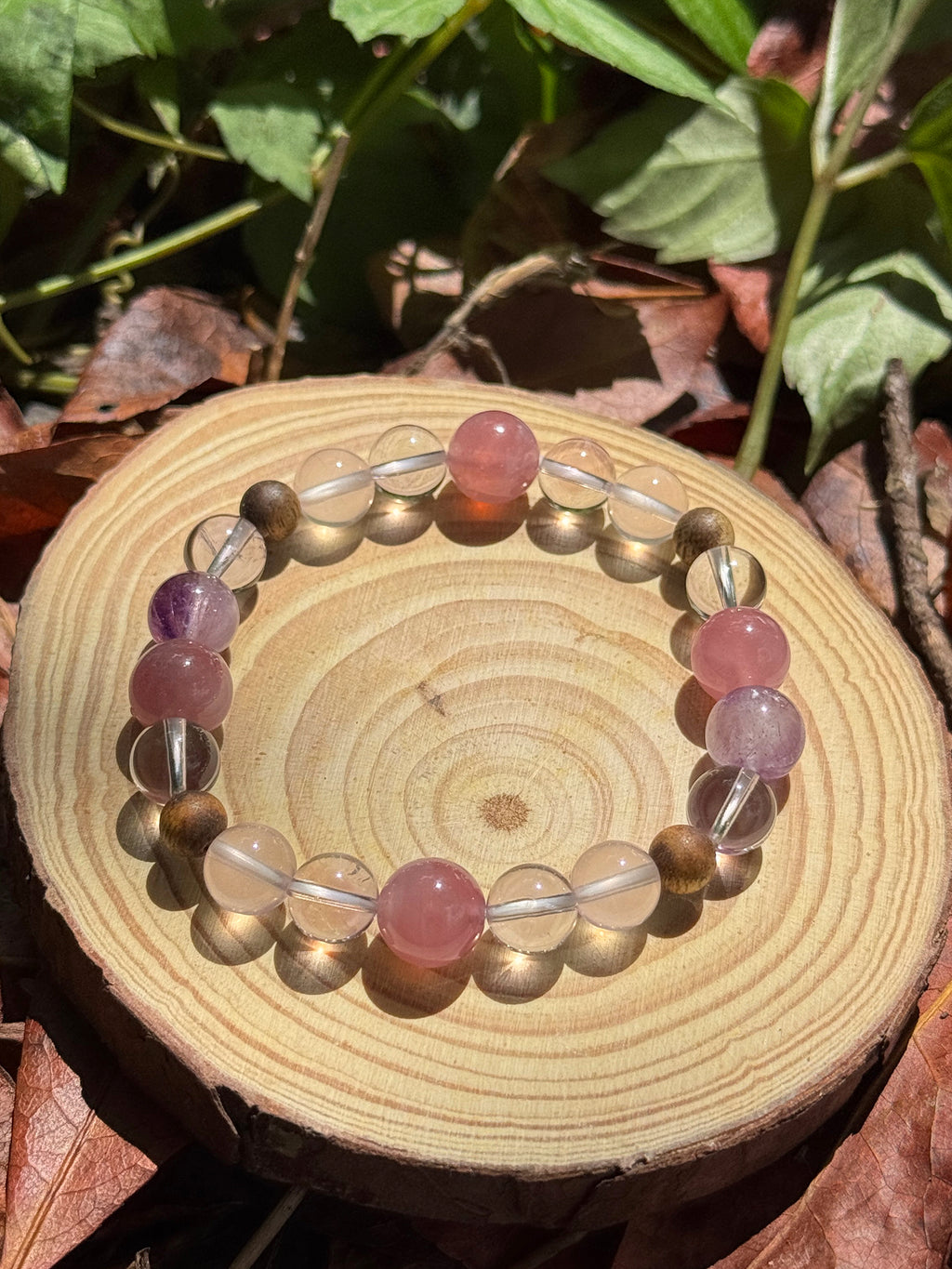 Natural rose quartz, Super Seven and agarwood bracelet photographed outdoors on grass in soft natural light