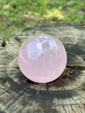 Natural rose quartz sphere displayed on a rustic wooden surface with soft pink tones, gentle translucency, and calming energy