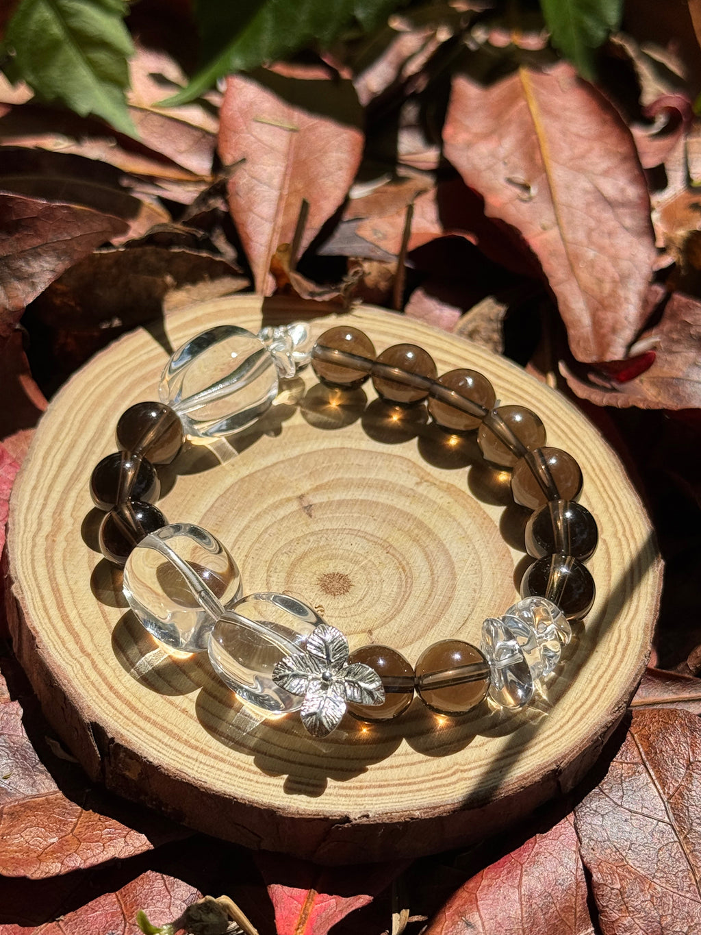 Natural smoky quartz and clear quartz bracelet photographed on grass under warm sunlight
