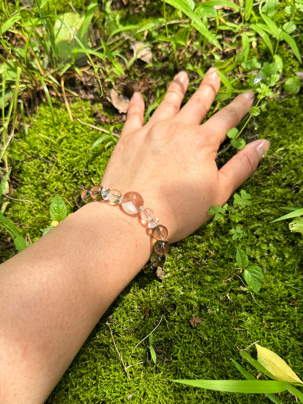 Smoky quartz and white phantom quartz bracelet worn on wrist close-up in natural sunlight