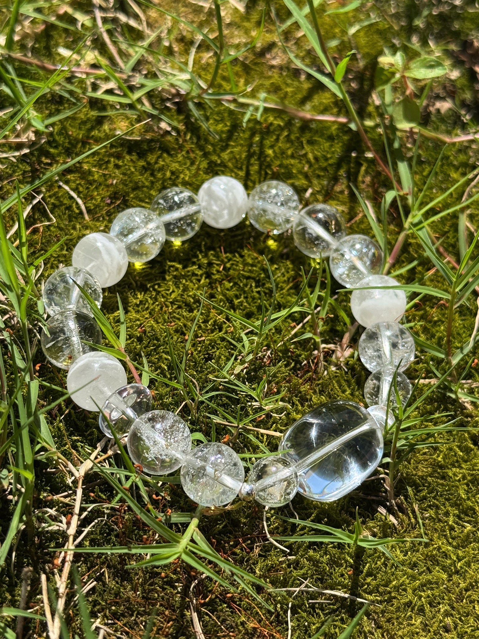 Natural White Phantom and Clear Quartz crystal bracelet with transparent beads, photographed outdoors on moss under natural sunlight.
